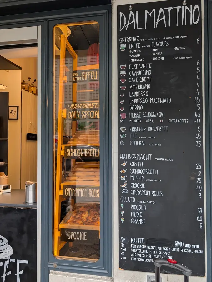 Schaufenster mit Kreidetafel „Dal Mattino“, Gipfeli und Zimtrollen im warmen Licht