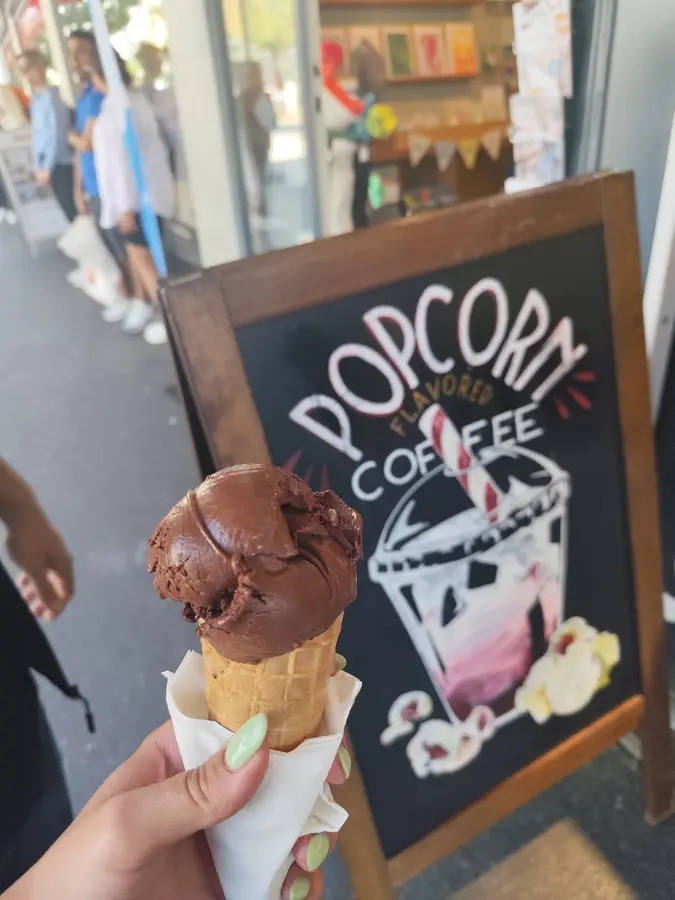 Schoggi-Glace im Cornet vor der Kreidetafel „Popcorn flavored Coffee“